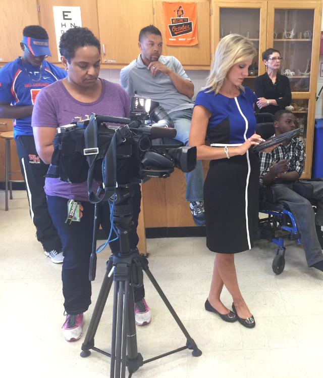 Los miembros del personal de Watkins Mill miran mientras Melissa Mollet de NBC4 filma una entrevista para su segmento sobre la recaudación de fondos de Chair4Ibra