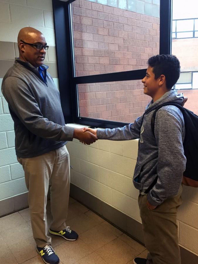 Assistant principal Eric Jackson and junior Leo Astorima shake hands in the hallway.