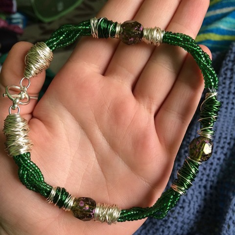 A handmade braided beaded anklet made by Serena Spickler. The small glass sequin beads are a deep green, paired with silver and green wire wrapping.