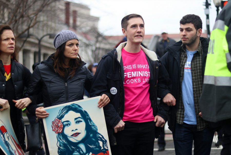 Mujeres + y + hombres + apoyando + al + artista + holding + de + marzo% 2C + Shepard + Fairelys + We + the + People + retratos + y + vistiendo + una + camiseta + feminista. +
