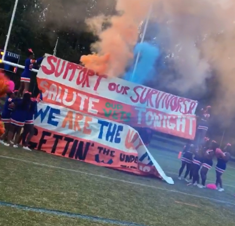 Rines football breaks through sign as they take the field. 