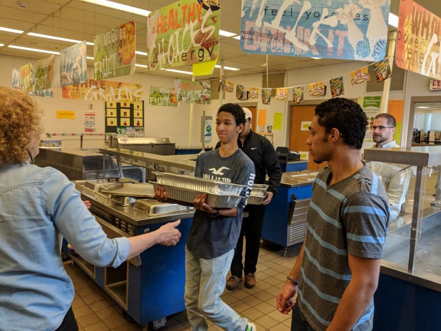 El estudiante de segundo año Fahad Habona y el estudiante de último año Ravi Bullard sirven almuerzos para el equipo de servicios del edificio