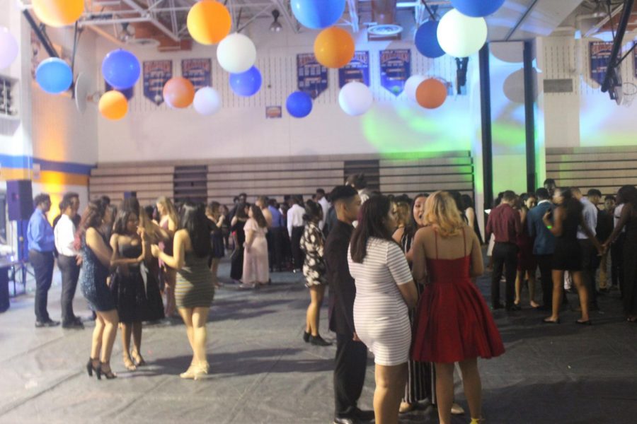 Students stand around with friends on the dance floor.